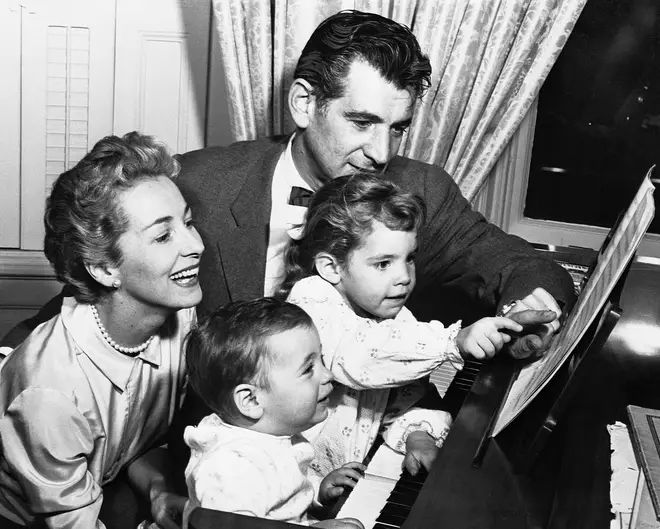 Leonard Bernstein plays piano with his sons, as wife Felicia looks on.