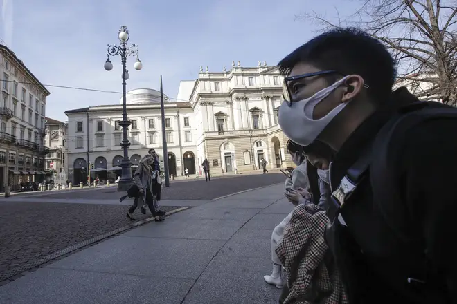 Locals wearing masks sit in front of La Scala opera house in Milan, Italy