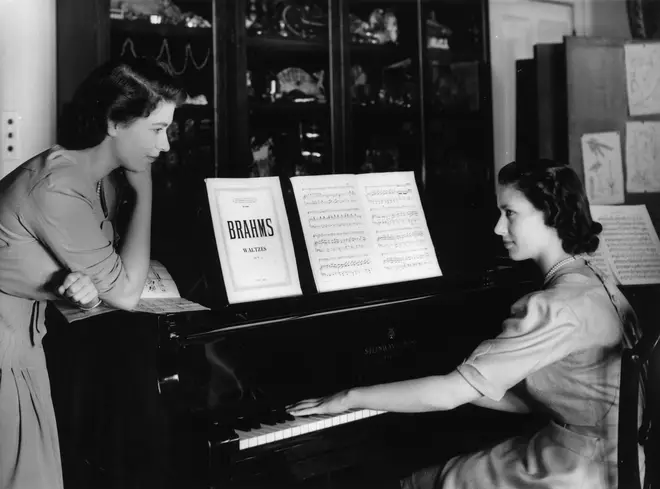 Princess Elizabeth watches her sister, Princess Margaret play a Brahms Waltz on the piano in the school room at Buckingham Palace.