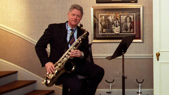 Bill Clinton poses in front of a Kenny G poster