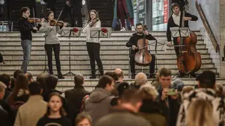 A string quintet performs in an underground train station being used as a bomb shelter