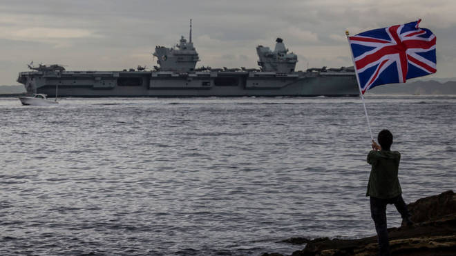 A British flag is raised as the British Royal Navy aircraft carrier HMS Queen Elizabeth sails out of a bay