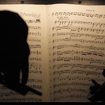 A silhouette of two violinists against sheet music.