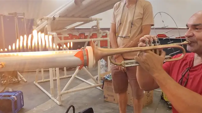 Moises Alves plays his trumpet into a rubber diaphragm at the end of a metal tube to visualise sound waves in the lit flames.