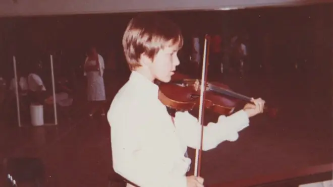 Adrian plays the violin as a boy